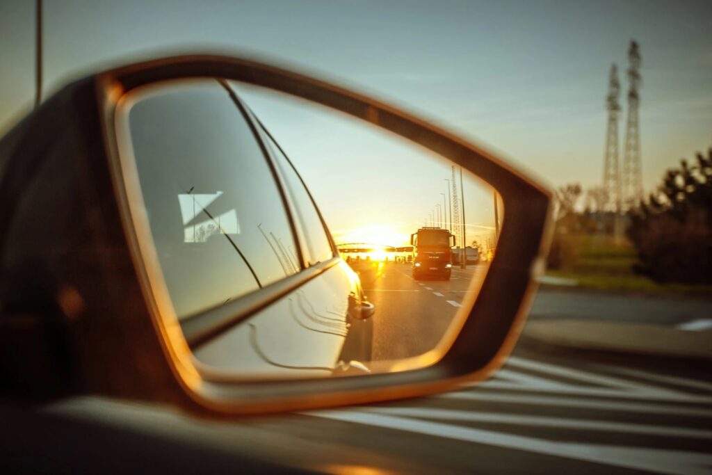 Rétroviseur extérieur d'une voiture reflétant la route et un camion au coucher du soleil